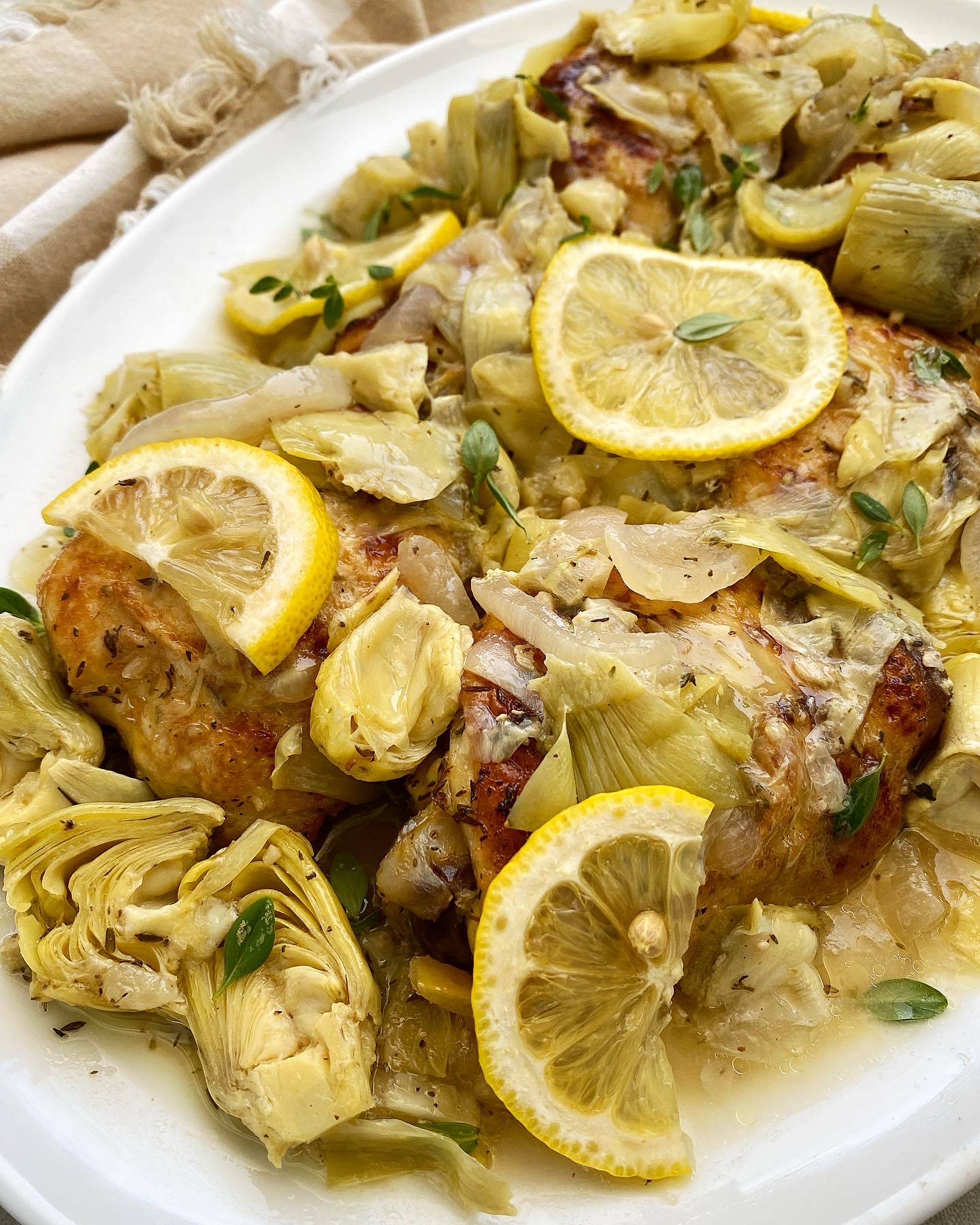 close up, side view of lemon artichoke chicken on a white plate with lemon slices and fresh thyme