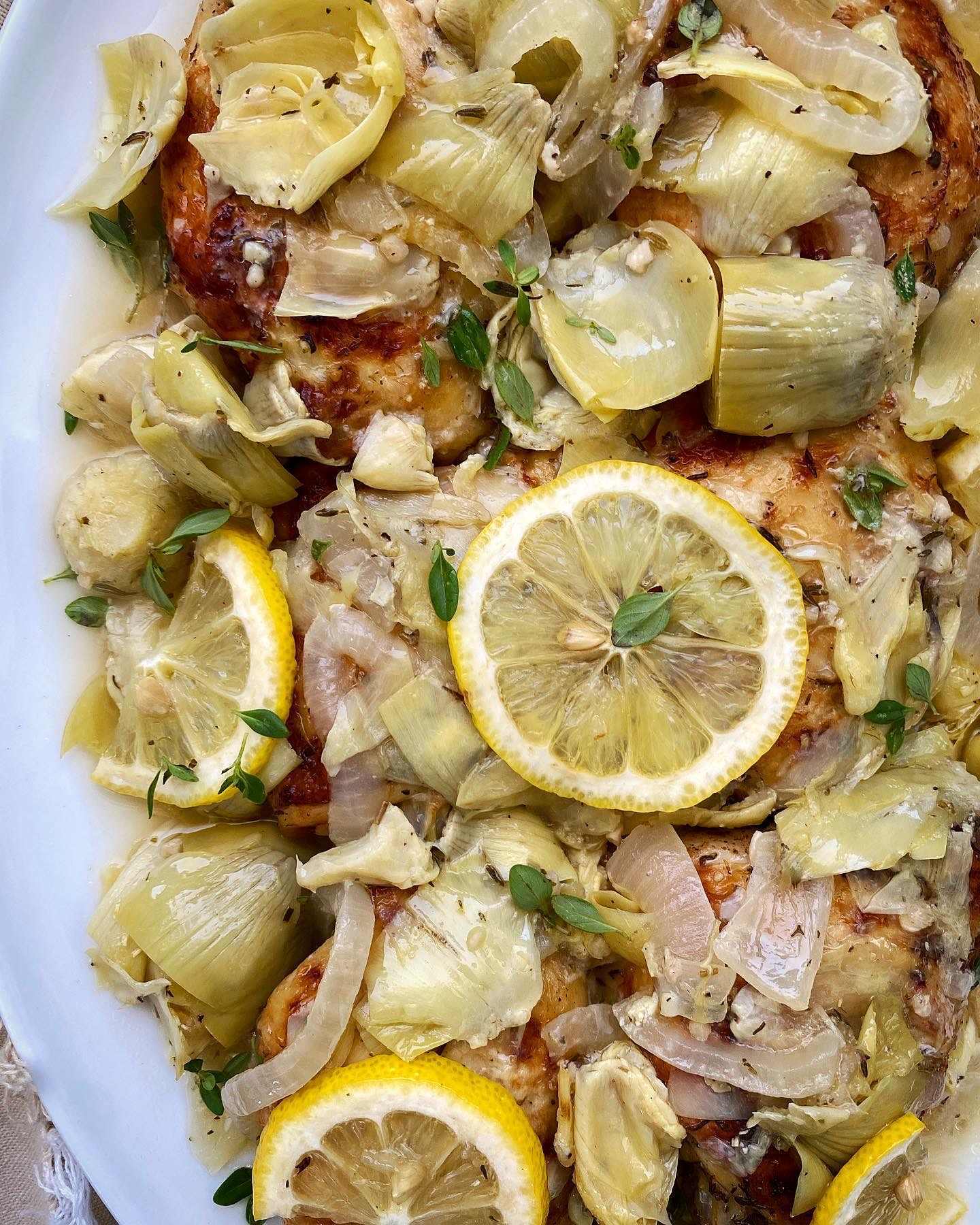close up of lemon artichoke chicken on a white plate with lemon slices and fresh thyme
