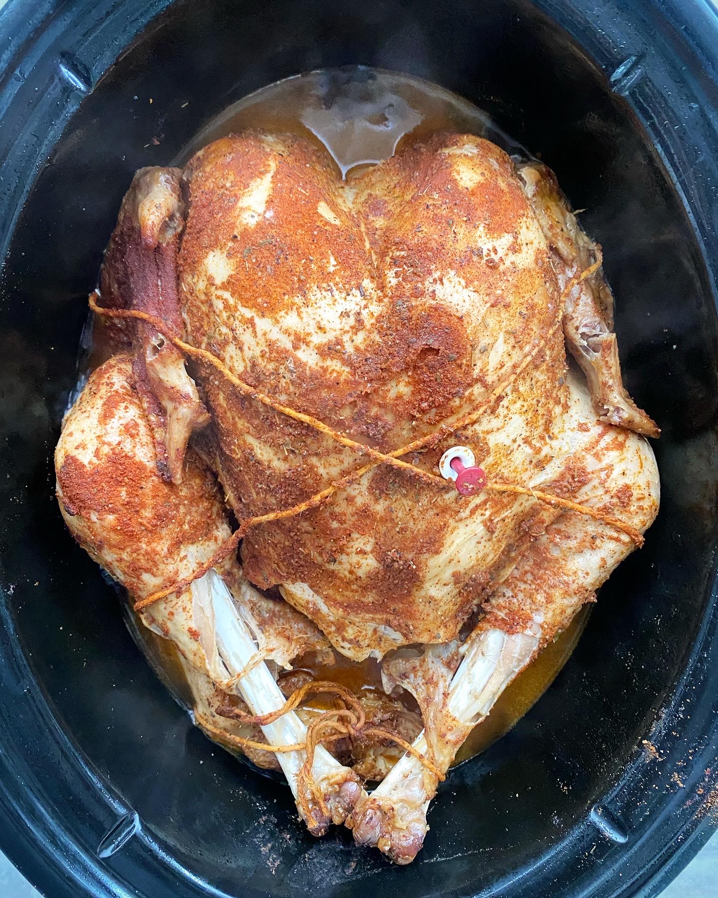 overhead shot of seasoned, cooked whole turkey in a black slow cooker