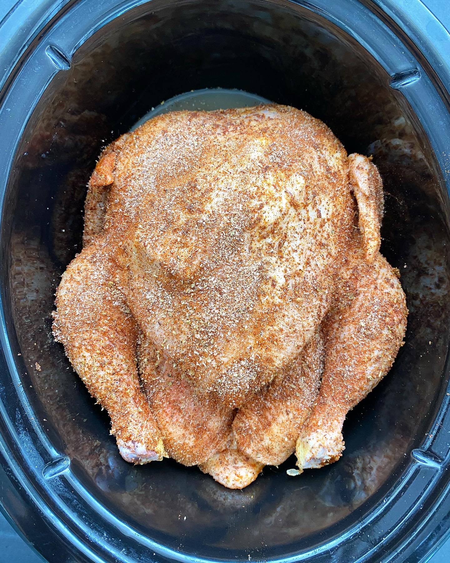 overhead shot of a uncooked whole chicken in a black slow cooker