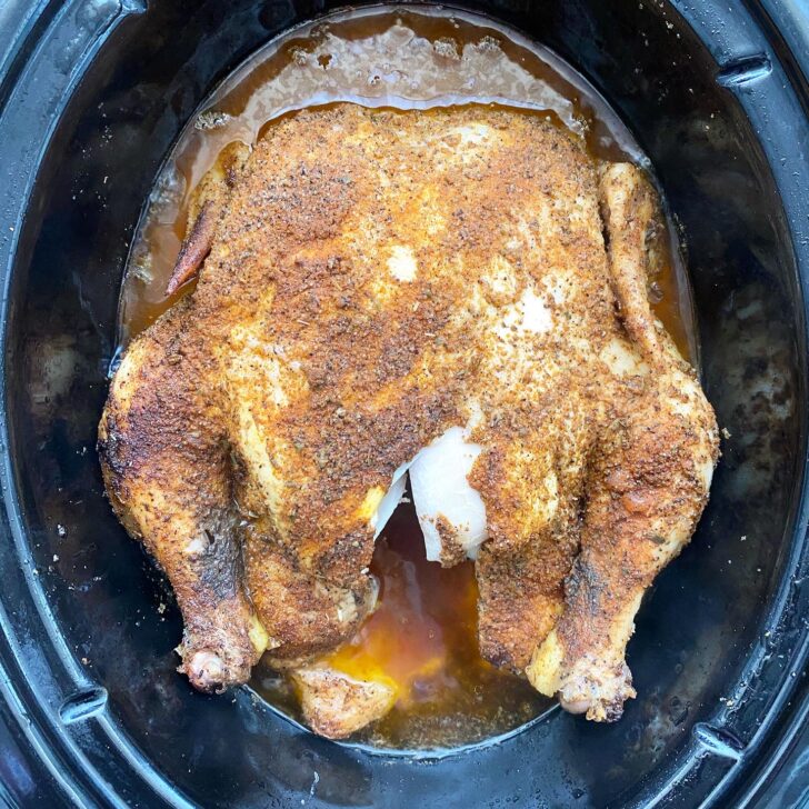 overhead shot of a cooked whole chicken in a black slow cooker