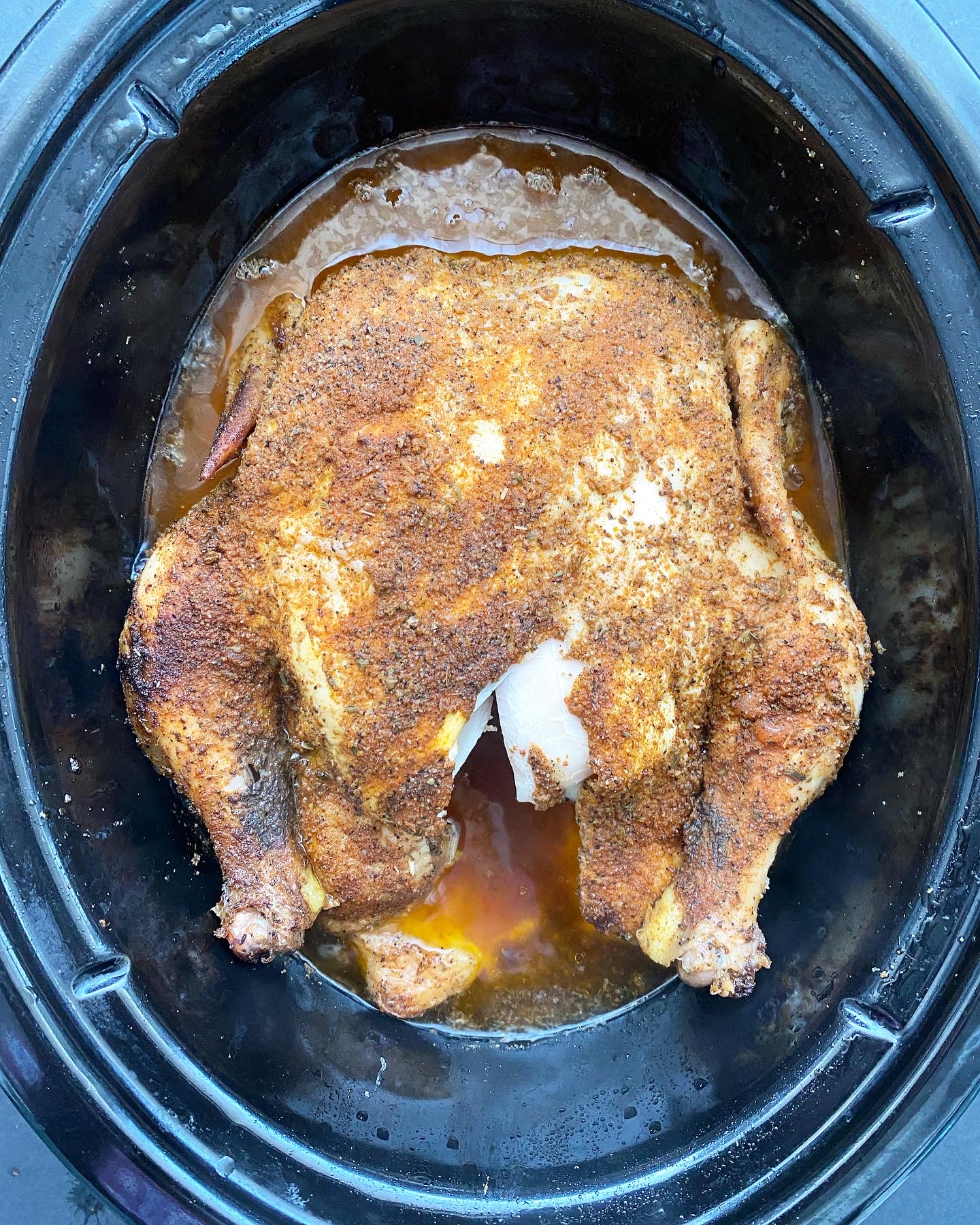 overhead shot of a cooked whole chicken in a black slow cooker