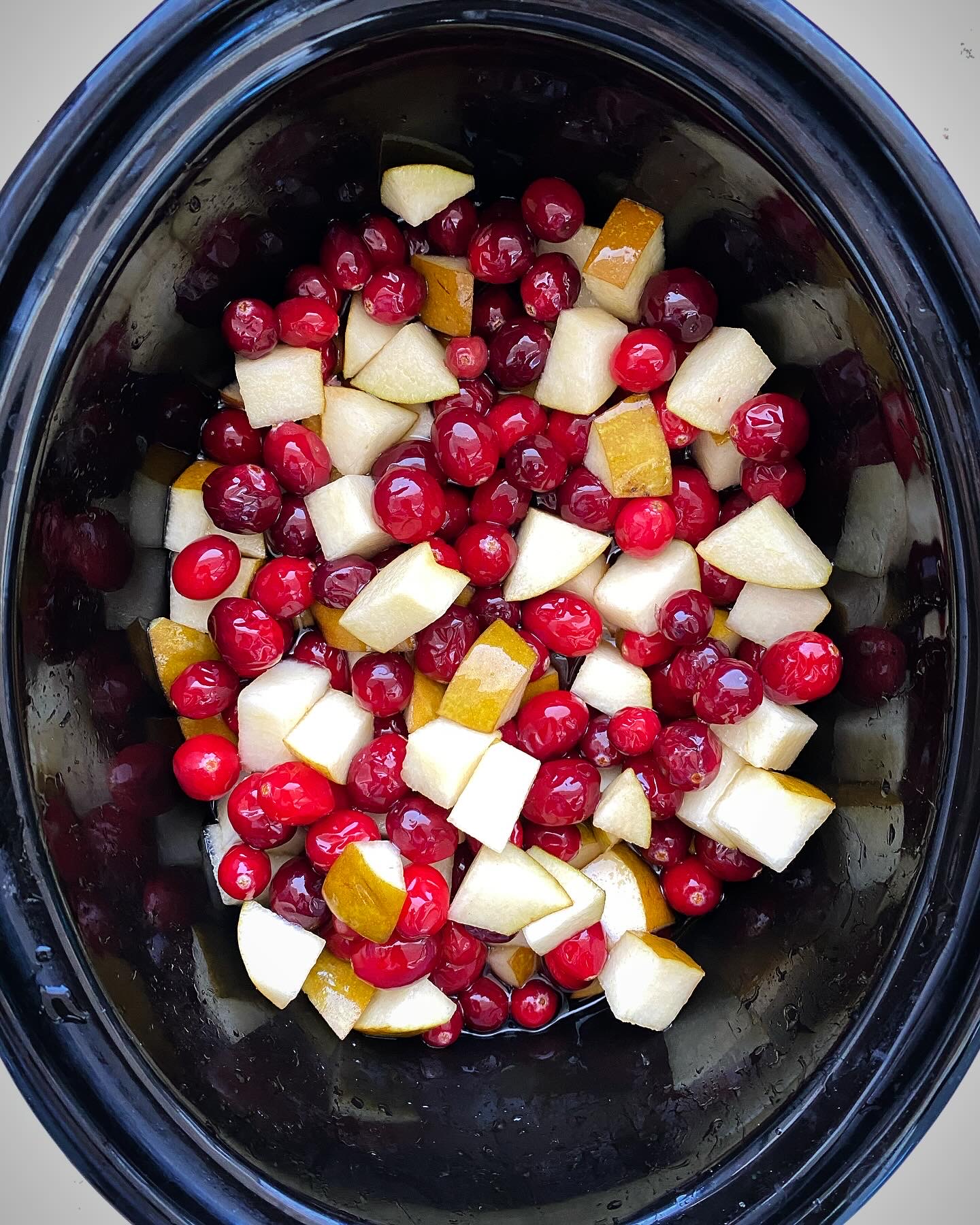 overhead shot of uncooked homemade cranberry sauce in a black slow cooker