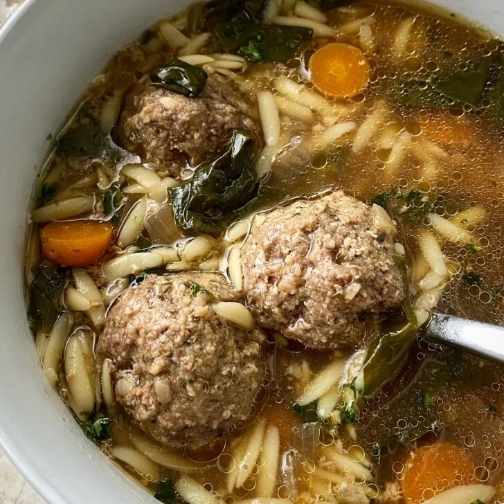 close up shot of Italian wedding soup in a white bowl with a silver spoon