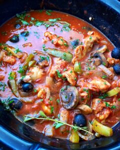 side view of cooked chicken cacciatore in the slow cooker with fresh herbs on top