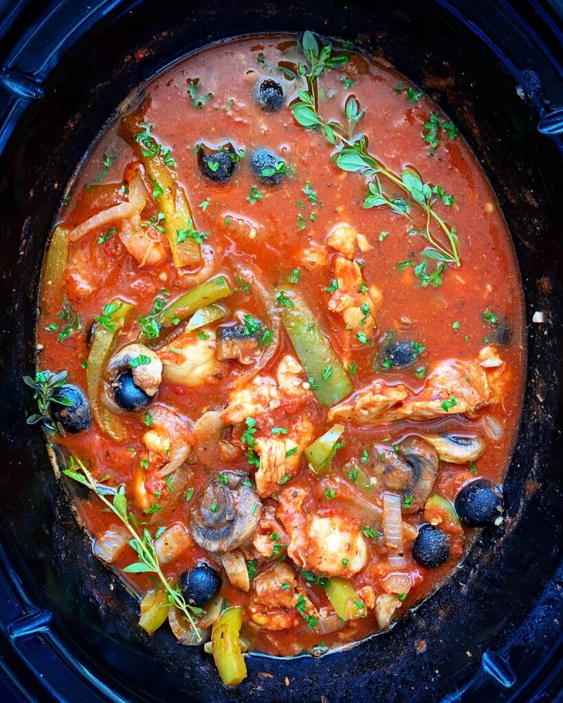cooked chicken cacciatore in the slow cooker with fresh herbs on top