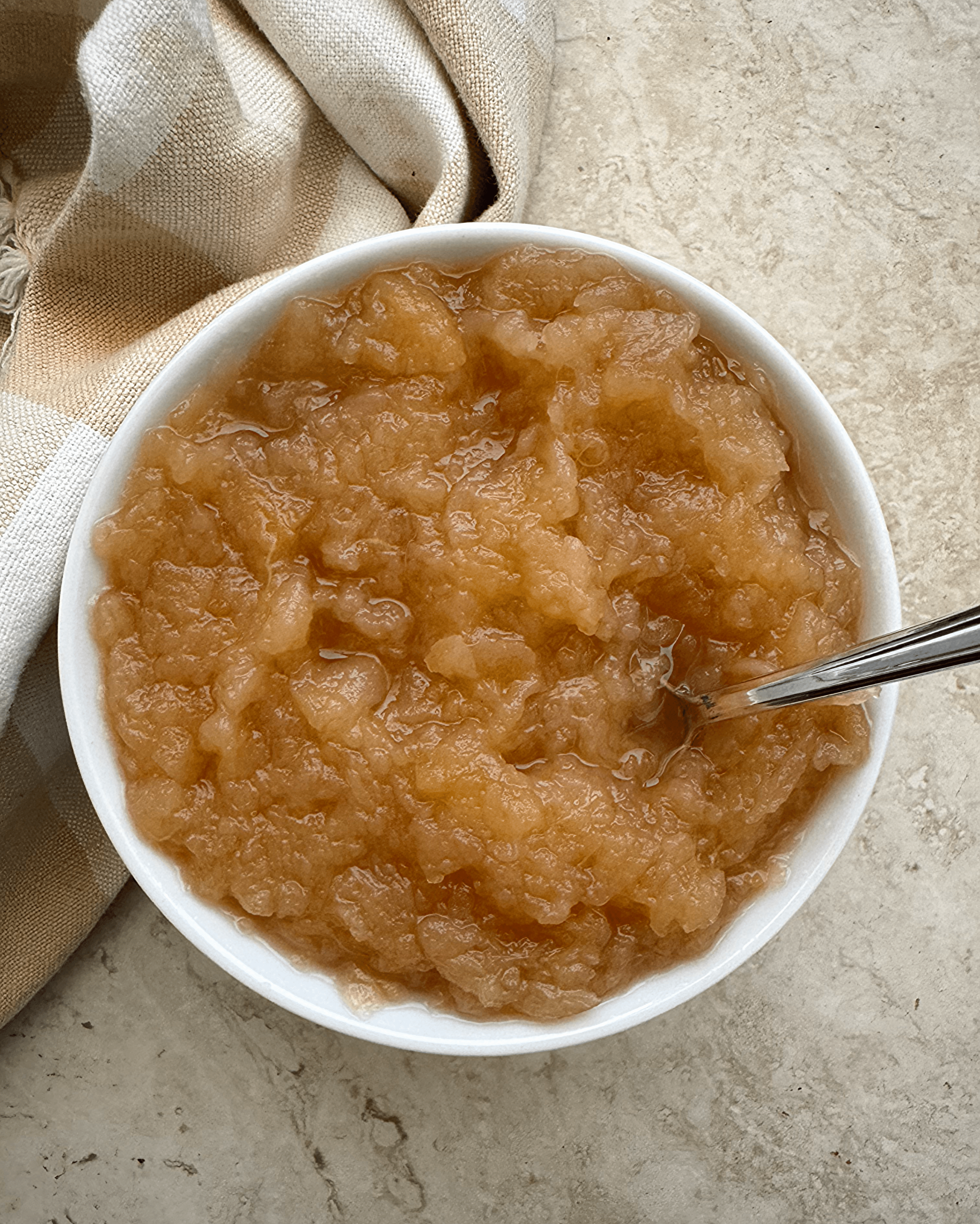 overhead shot of unsweetened applesauce in a white bowl with a silver spoon