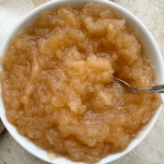 overhead shot of unsweetened applesauce in a white bowl with a silver spoon