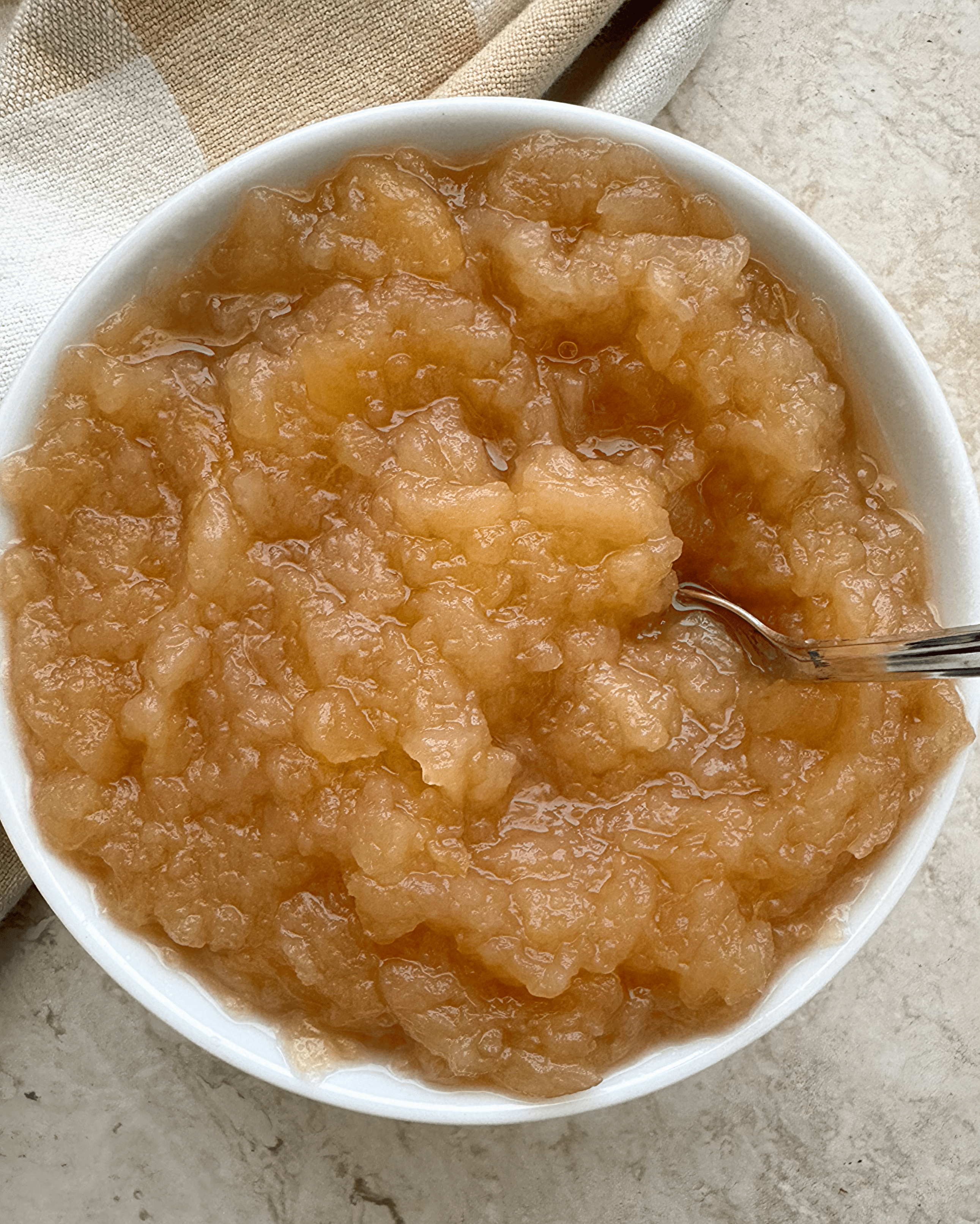 overhead shot of unsweetened applesauce in a white bowl with a silver spoon