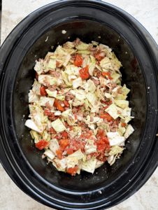 overhead shot of uncooked slow cooker unstuffed cabbage rolls in a black slow cooker