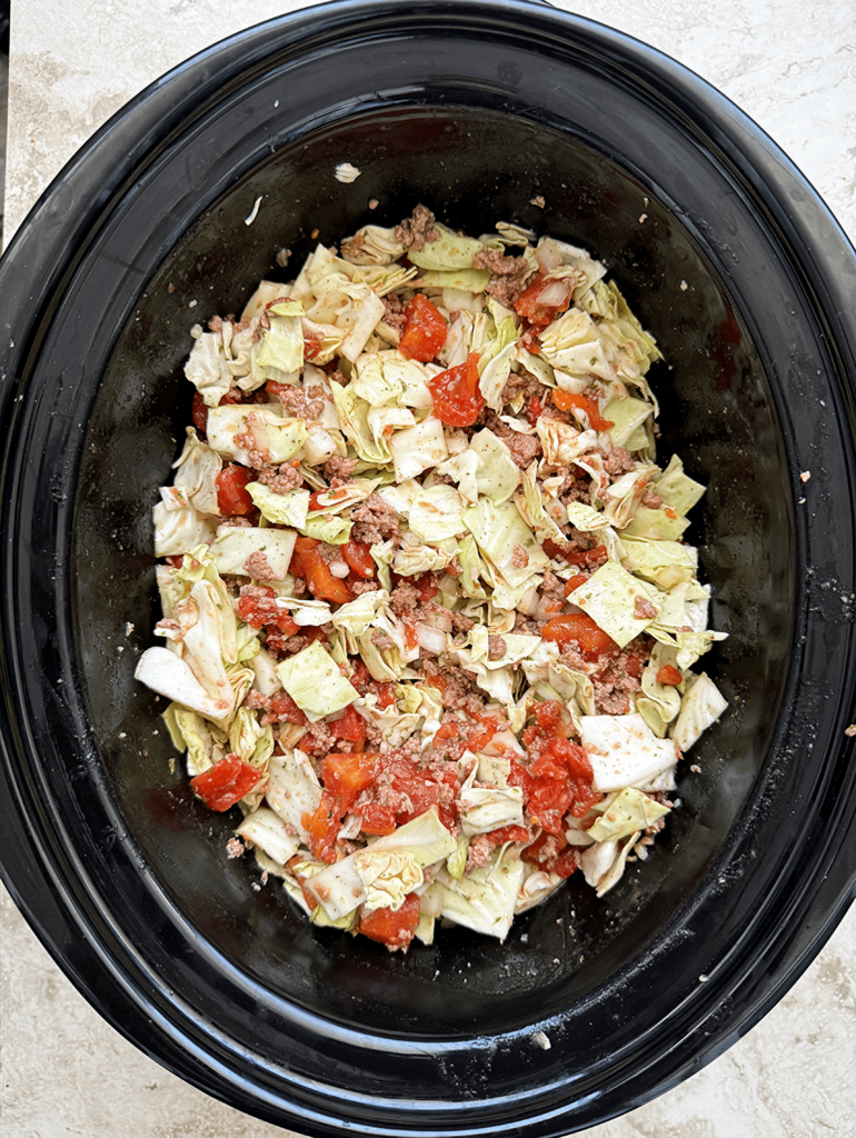overhead shot of uncooked slow cooker unstuffed cabbage rolls in a black slow cooker