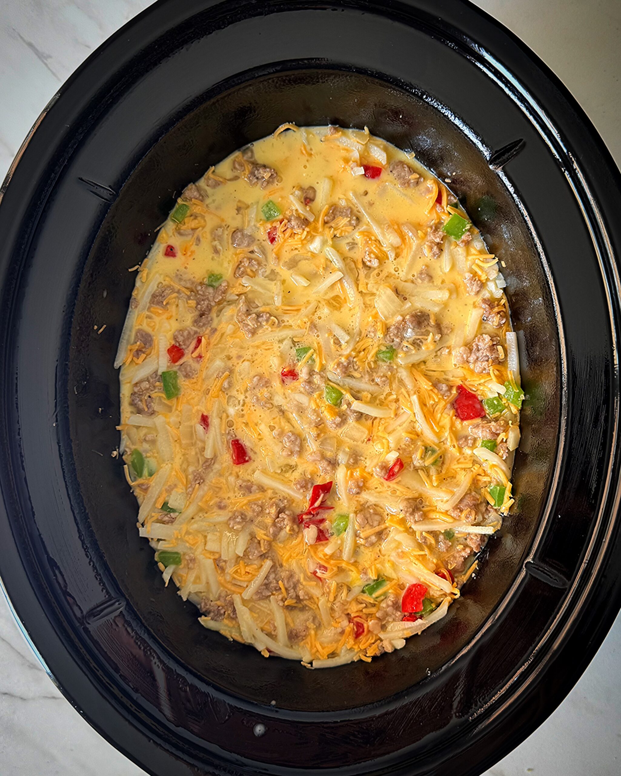 overhead shot of uncooked breakfast casserole in a black slow cooker
