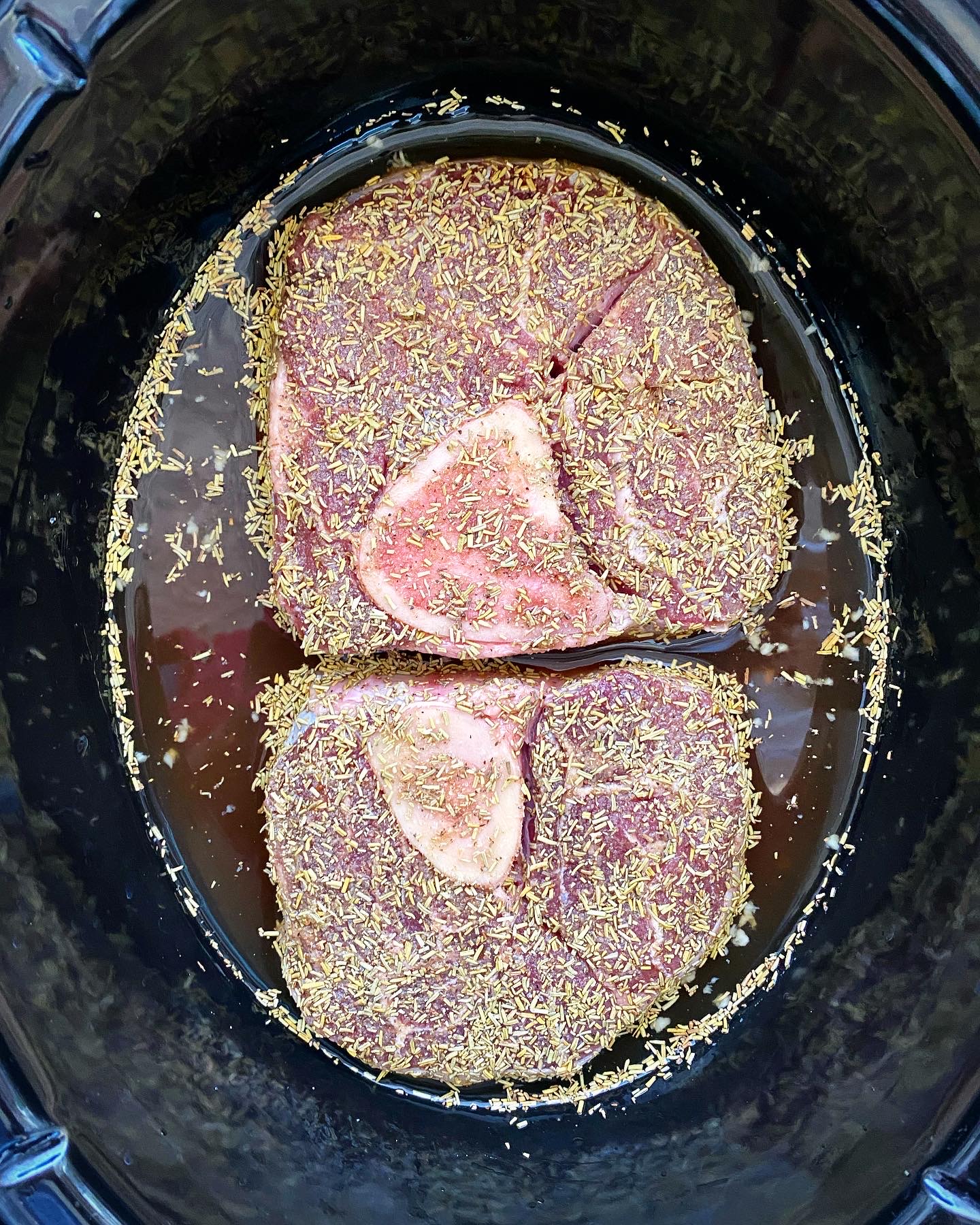 overhead shot of seasoned, uncooked beef shanks in a black crockpot