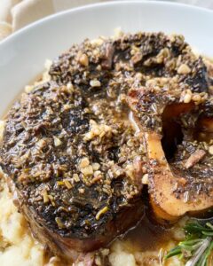 close up, side view shot of a beef shank served over mashed cauliflower in a white bowl