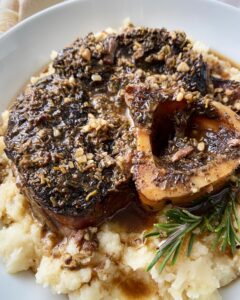 close up, side view shot of a beef shank served over mashed cauliflower in a white bowl
