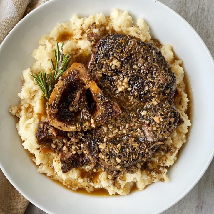overhead shot of garlic herb beef shanks served over mashed cauliflower in a white bowl