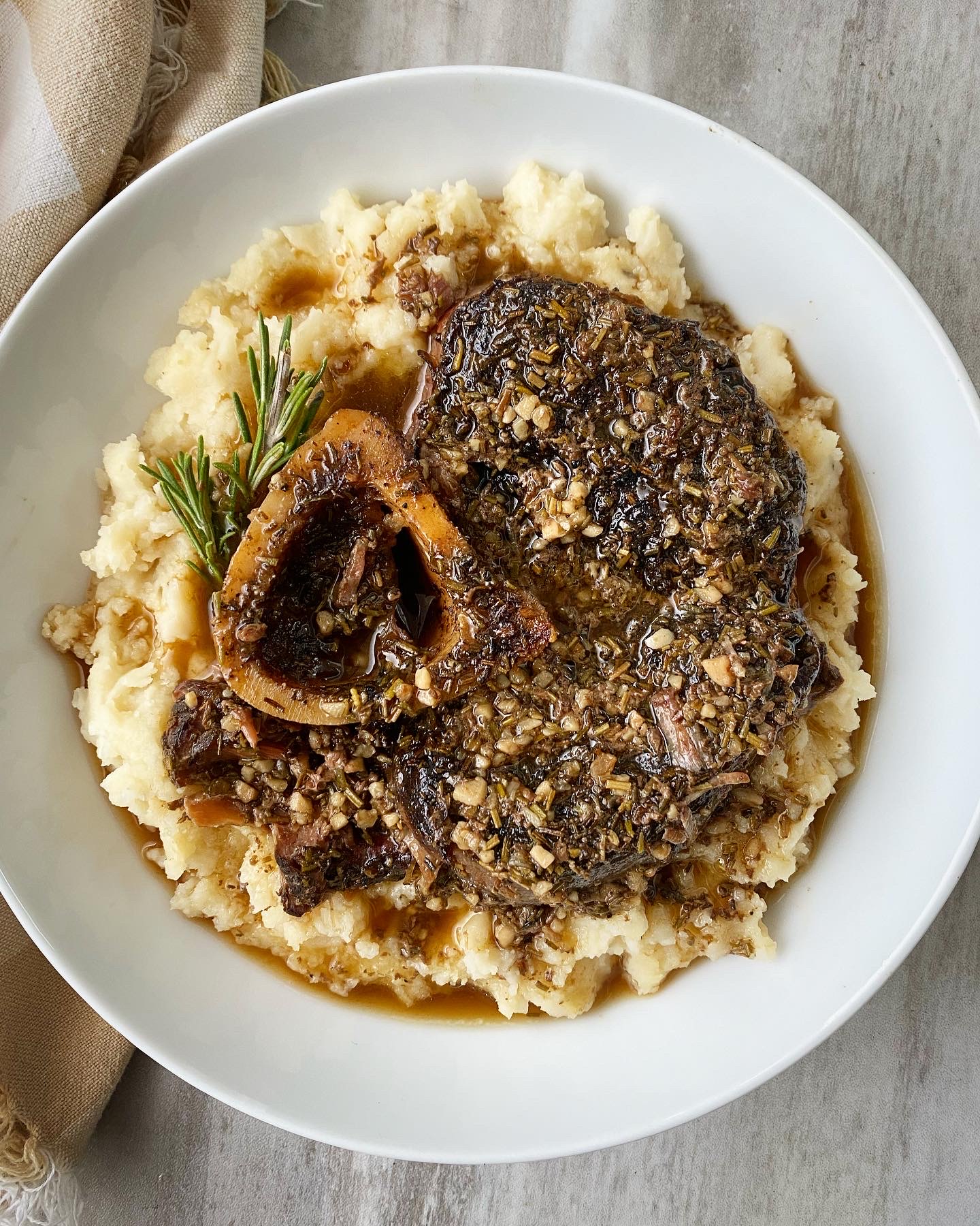 overhead shot of garlic herb beef shanks served over mashed cauliflower in a white bowl