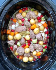 overhead shot of uncooked cranberry beef stew in a black slow cooker
