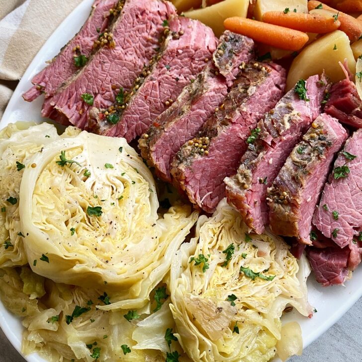 close up shot of corned beef & cabbage with potatoes, carrots, and onion on a white platter
