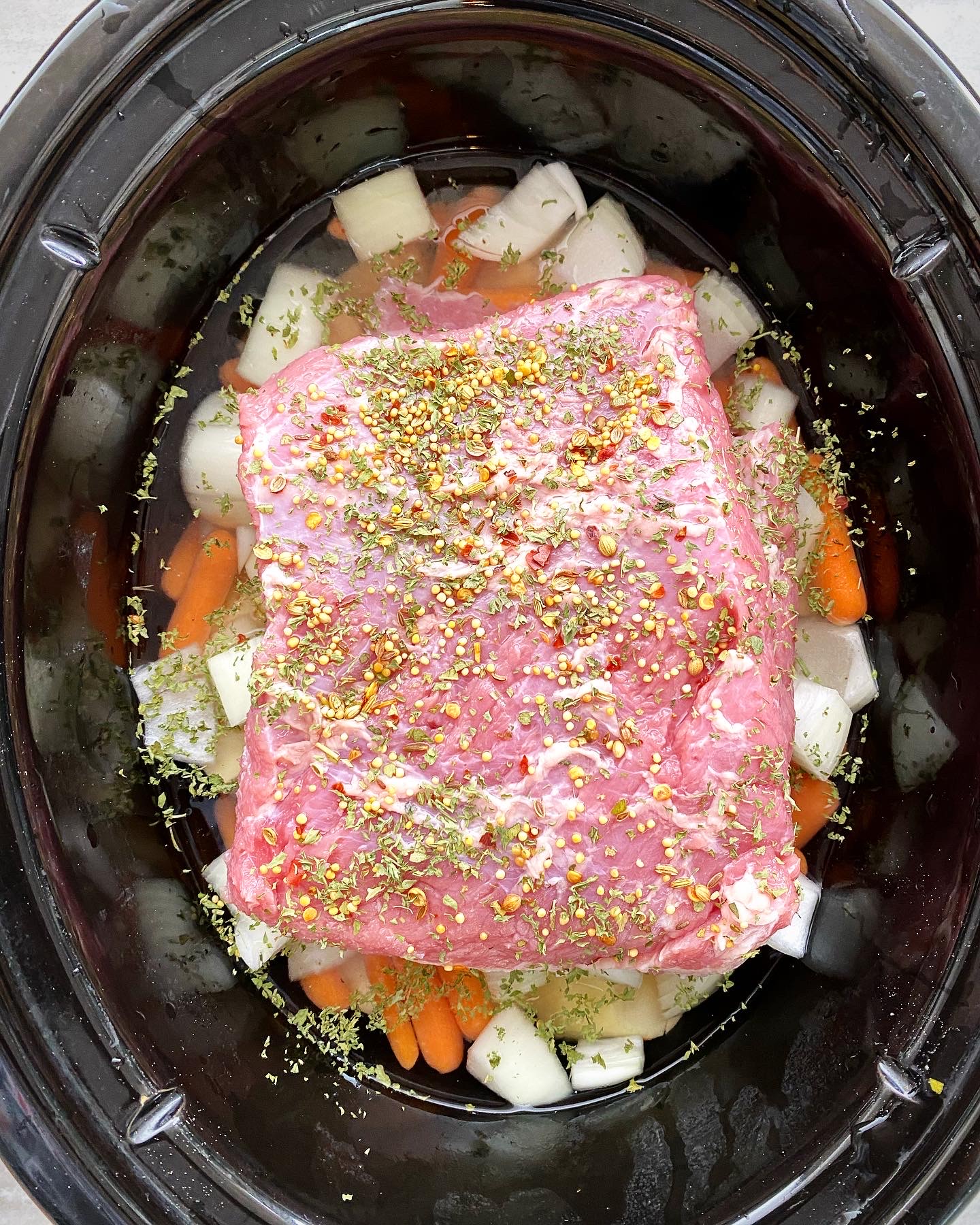 overhead shot of uncooked corned beef with potatoes, carrots, and onion in a black slow cooker