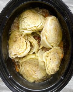 overhead shot of cooked corned beef with potatoes, carrots, and onion in a black slow cooker with cooked cabbage wedges on top