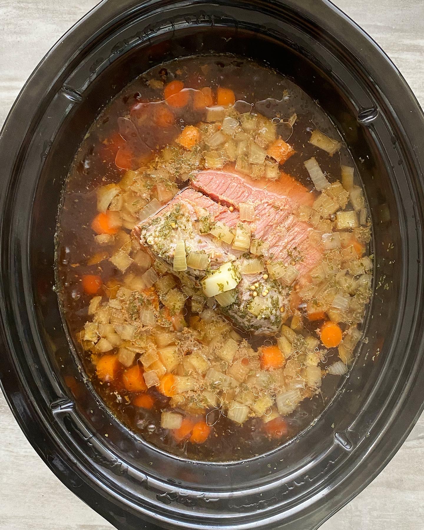 overhead shot of cooked corned beef & cabbage soup in a black slow cooker