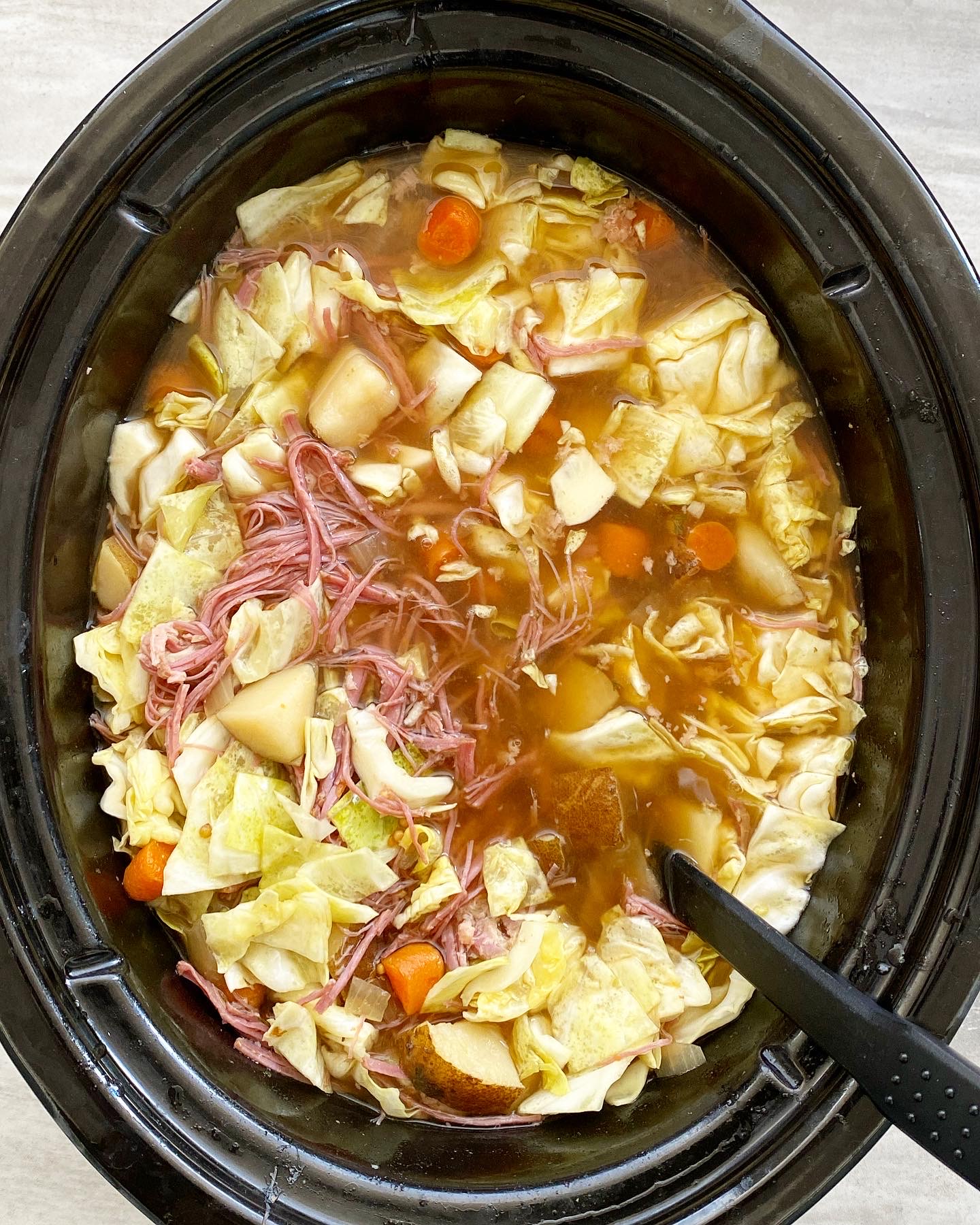 overhead shot of cooked corned beef & cabbage soup in a black slow cooker with cabbage