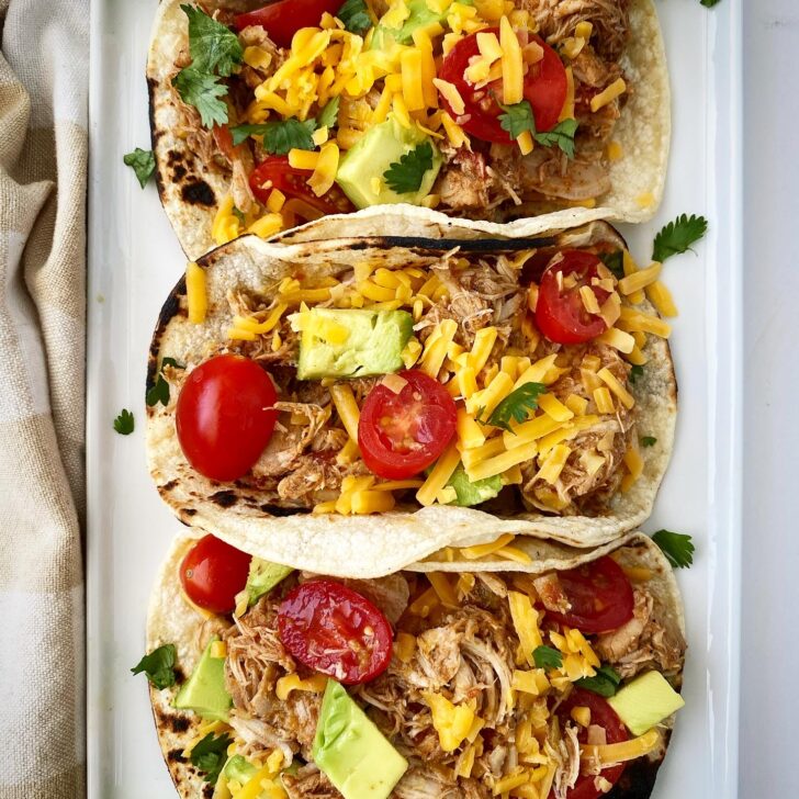 overhead shot of easy crockpot chicken tacos in tortillas on a white plate