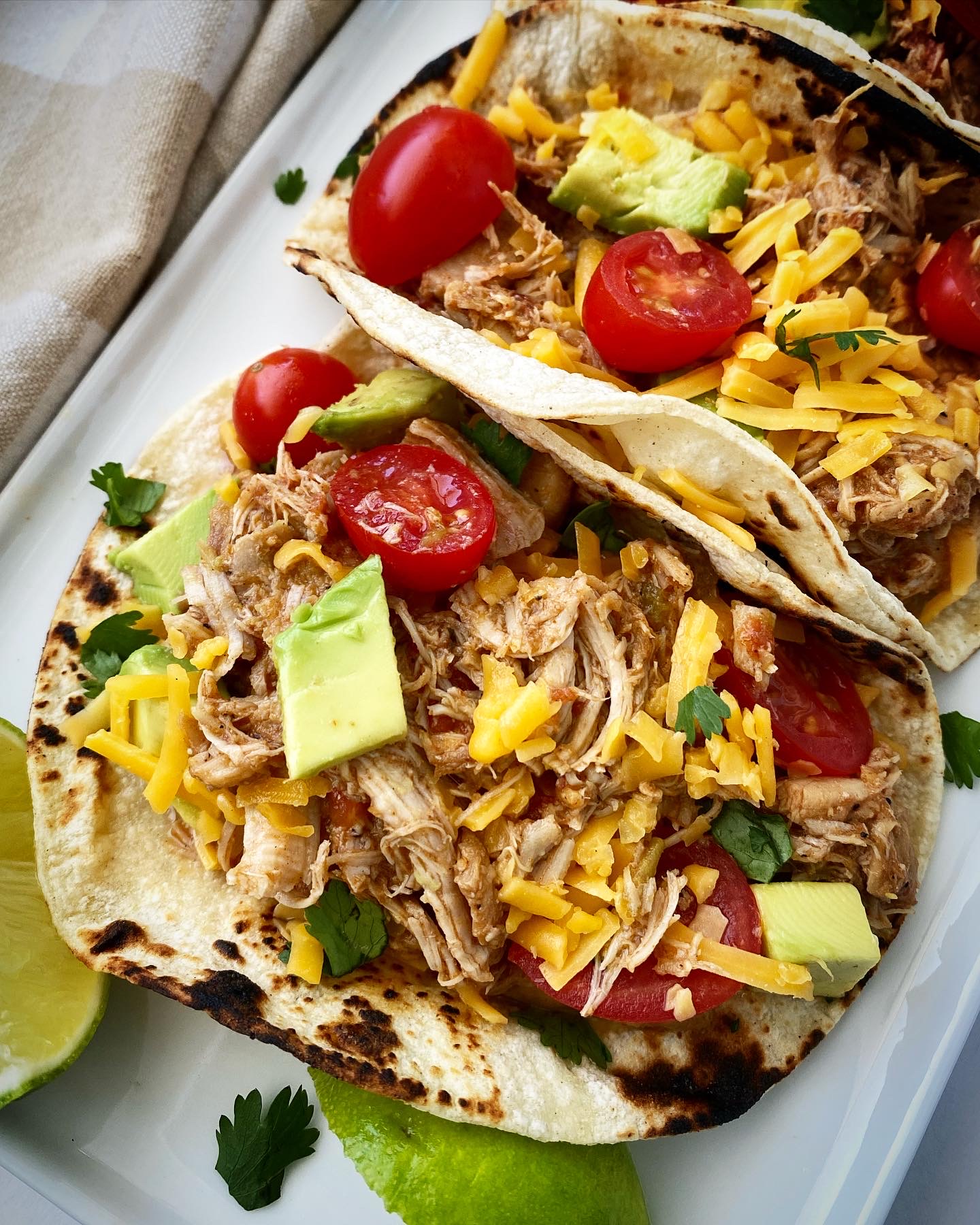 close up shot of easy crockpot chicken tacos in tortillas on a white plate