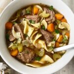 overhead shot of cooked beef noodle soup in a white bowl with a silver spoon