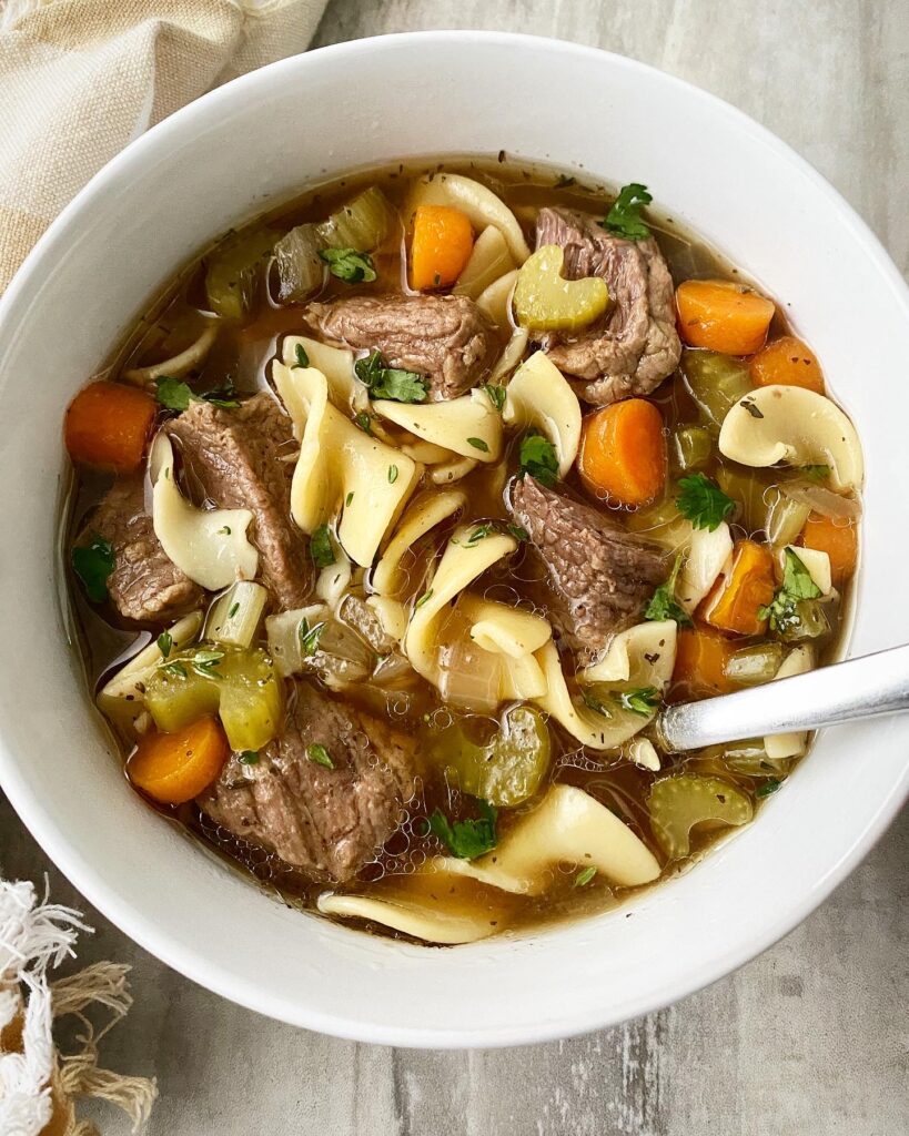 overhead shot of cooked beef noodle soup in a white bowl with a silver spoon