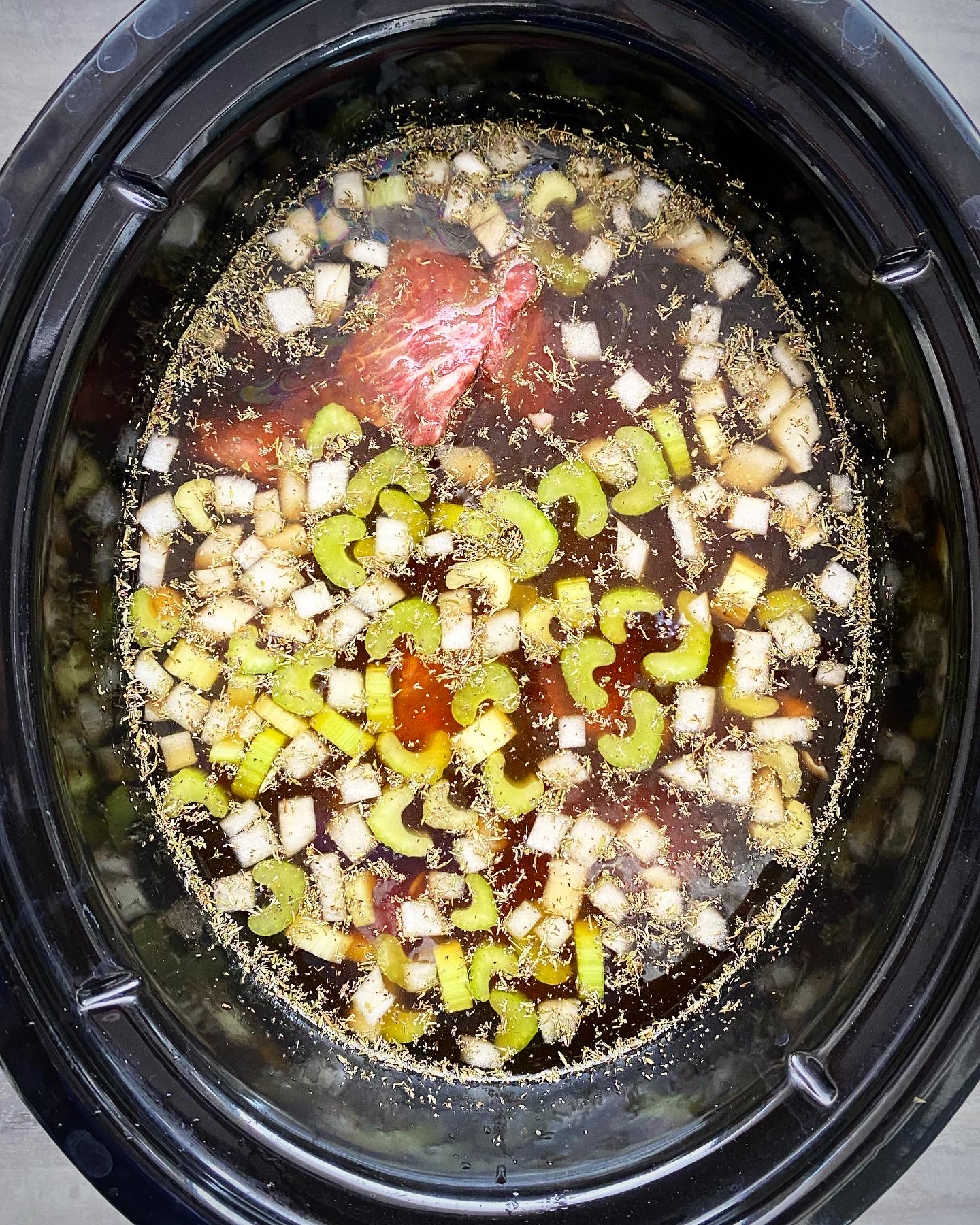 overhead shot of uncooked beef noodle soup in a black slow cooker