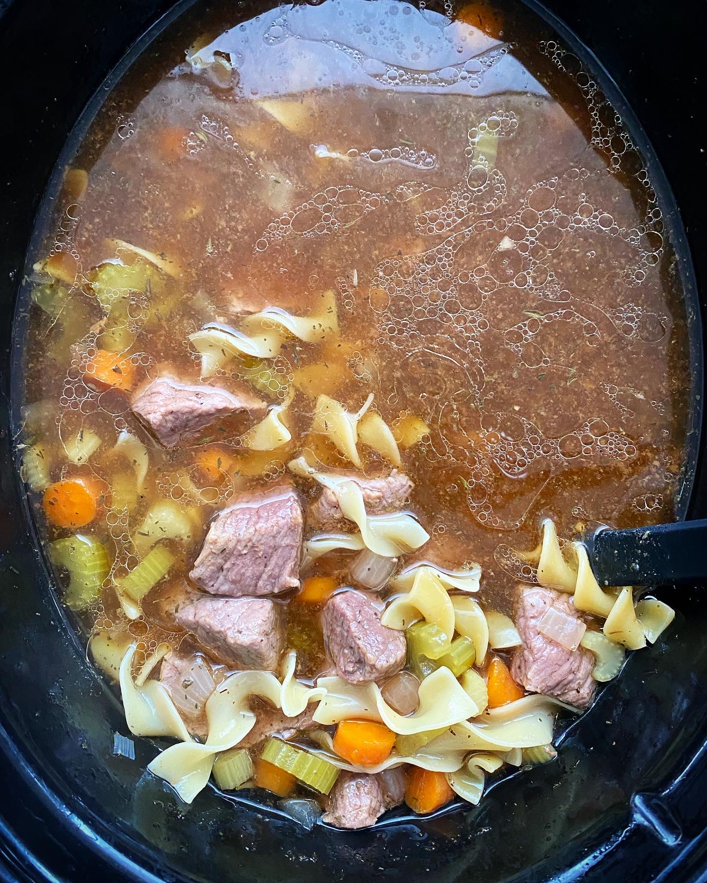 overhead shot of cooked beef noodle soup in a black slow cooker