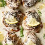 close up, overhead shot of crockpot creamy lemon dill chicken on a white platter garnished with lemon slices & fresh dill