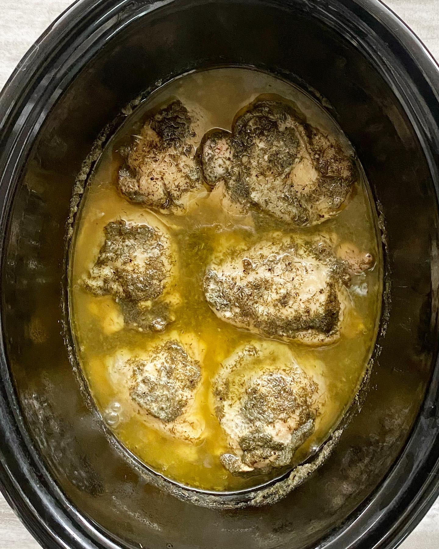 overhead shot of cooked creamy lemon dill chicken in a black slow cooker