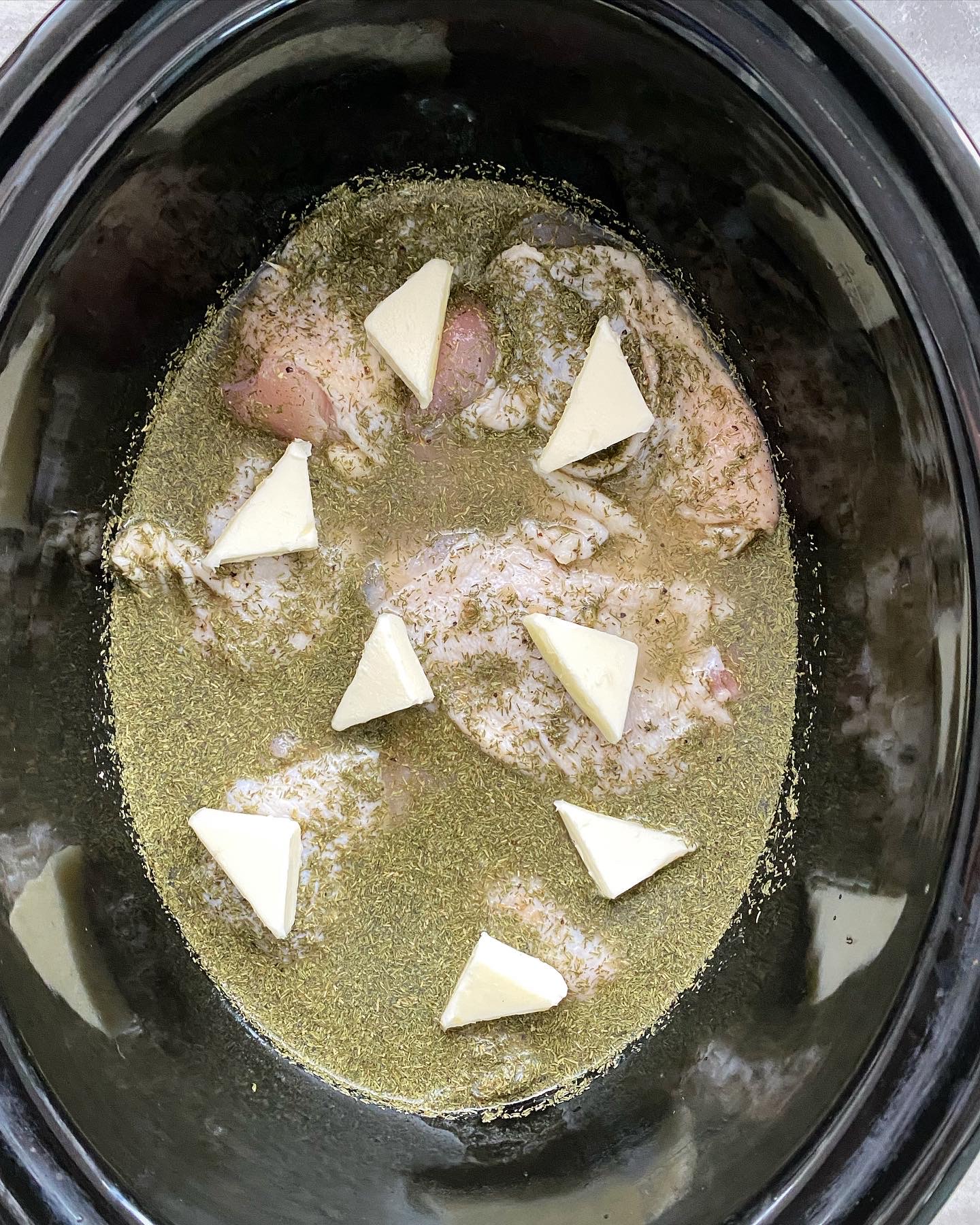overhead shot of uncooked creamy lemon dill chicken in a black slow cooker