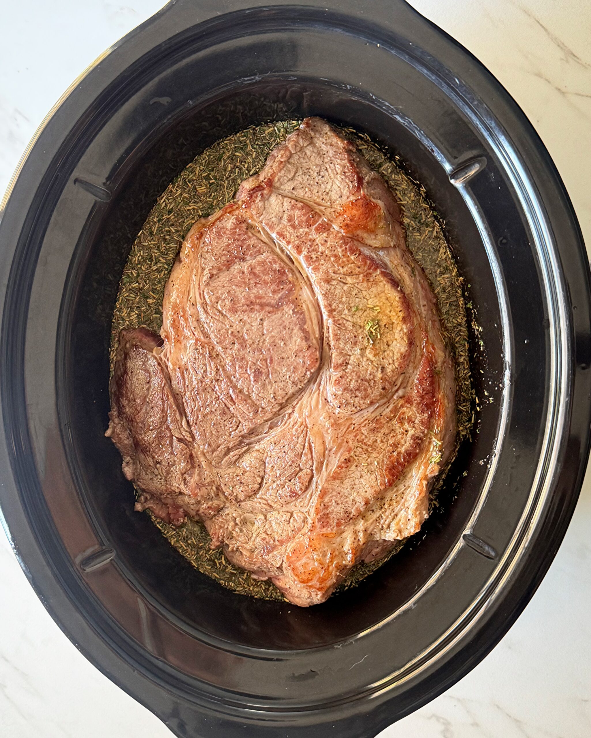overhead shot of uncooked chuck roast in a black slow cooker