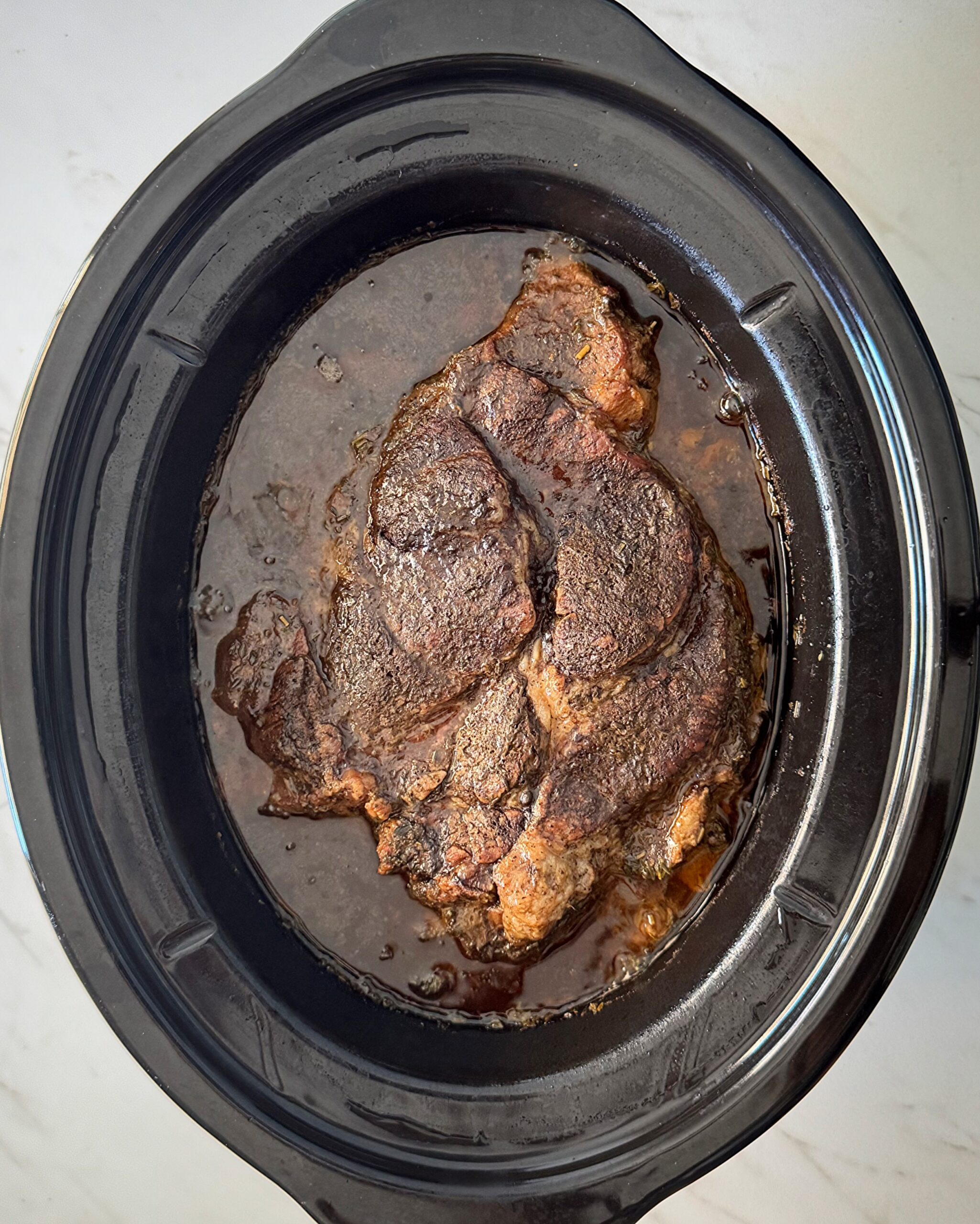 overhead shot of cooked chuck roast in a black slow cooker