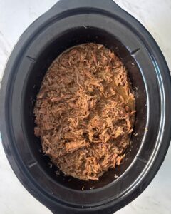 overhead shot of cooked, shredded chuck roast in a black slow cooker