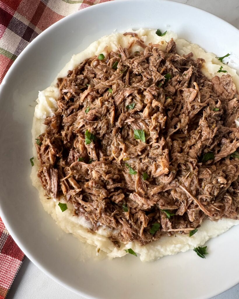 overhead shot of shredded beef served over mashed potatoes on a white plate