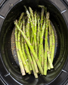 overhead shot of uncooked close up shot of Slow Cooker Lemon Garlic Asparagus in a black slow cooker