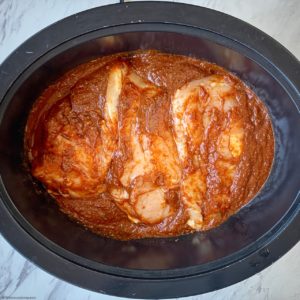 overhead shot of uncooked BBQ pulled chicken in a black slow cooker