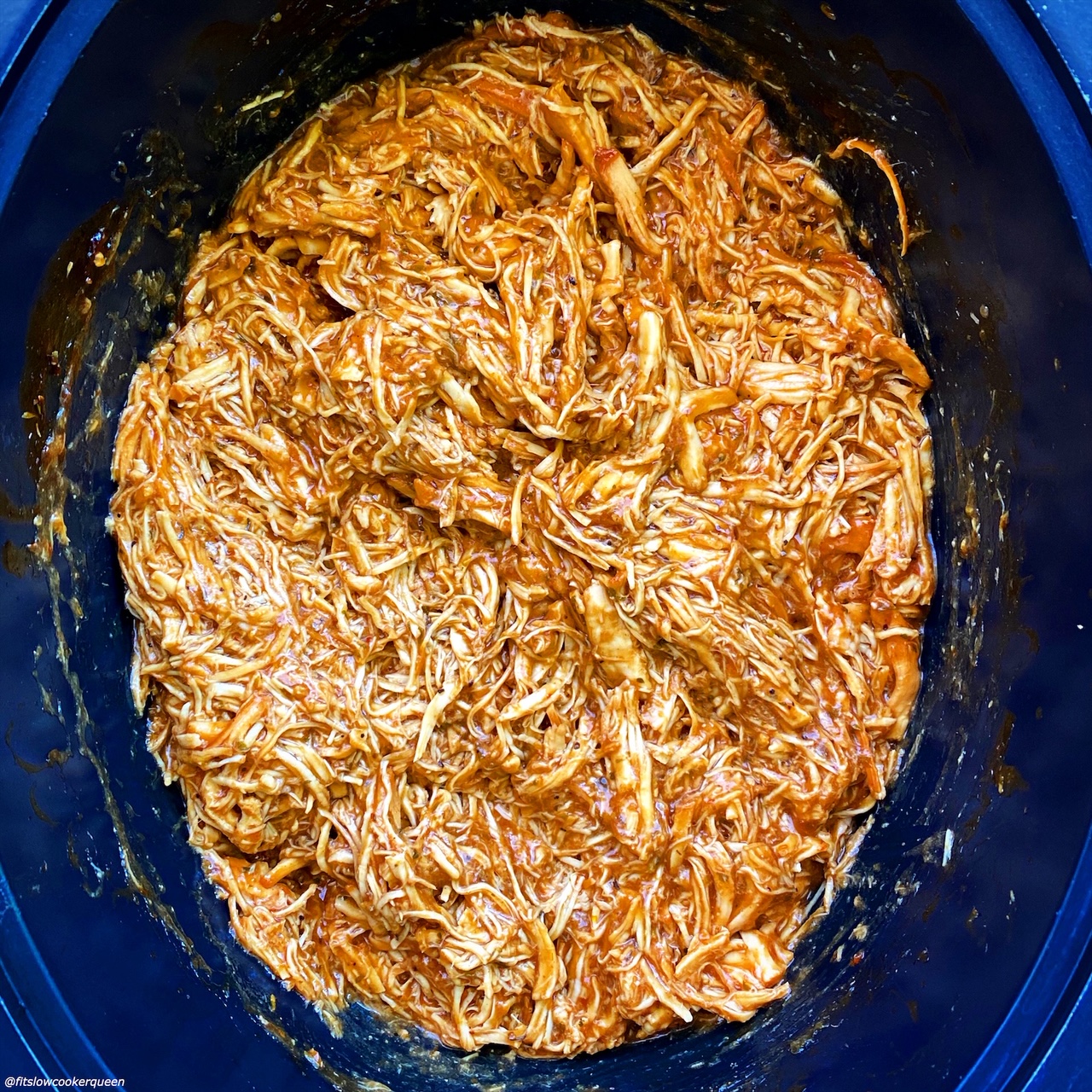 overhead shot of cooked, shredded BBQ pulled chicken in a black slow cooker