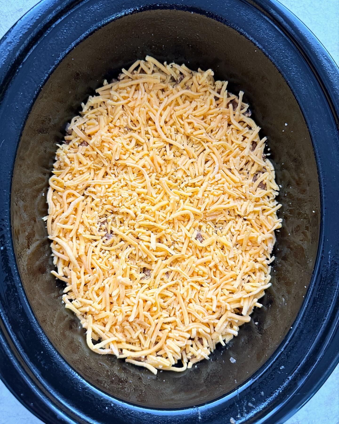 overheaed shot of uncooked cheeseburger casserole in a black slow cooker