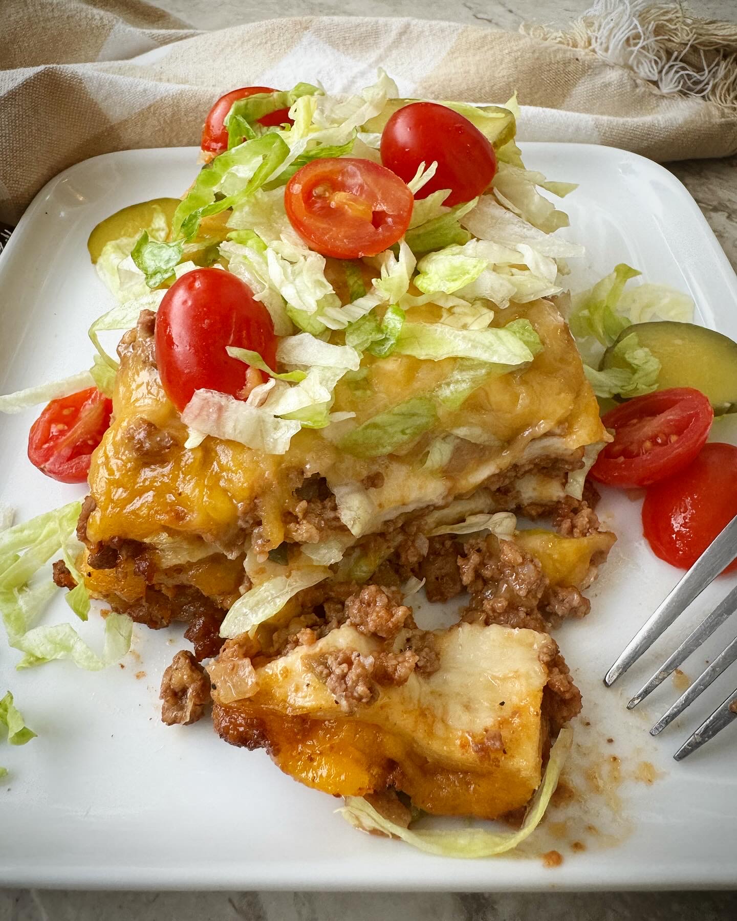 close up shot of a slice of cheeseburger casserole in a black slow cooker garnished with shredded lettuce, pickles, and diced tomatoes