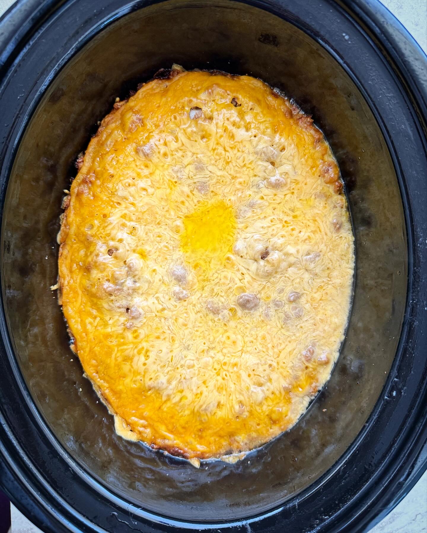 overheaed shot of cooked cheeseburger casserole in a black slow cooker