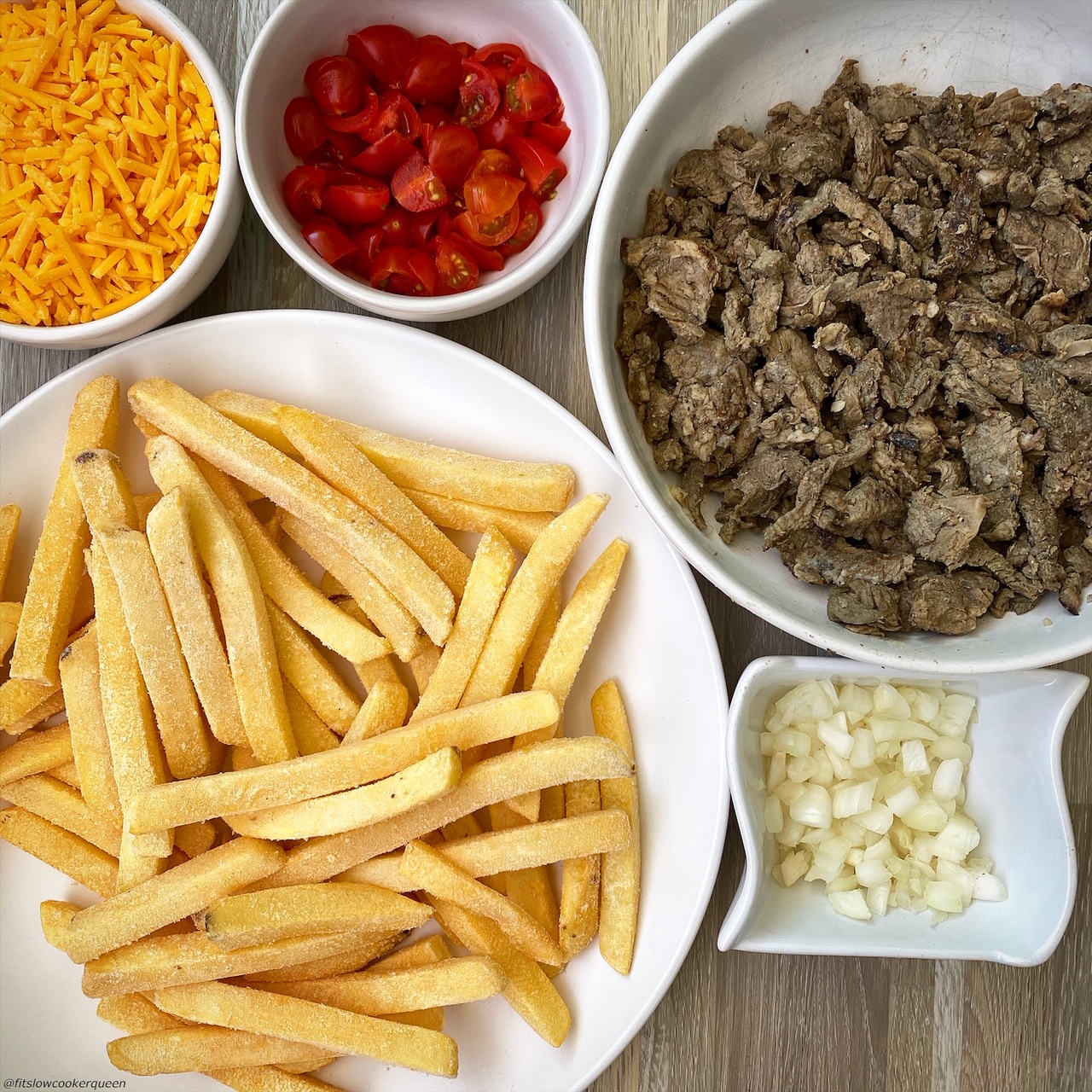 frozen french fries, cooked carne asada, shredded cheddar cheese, tomatoes, and onions in bowl