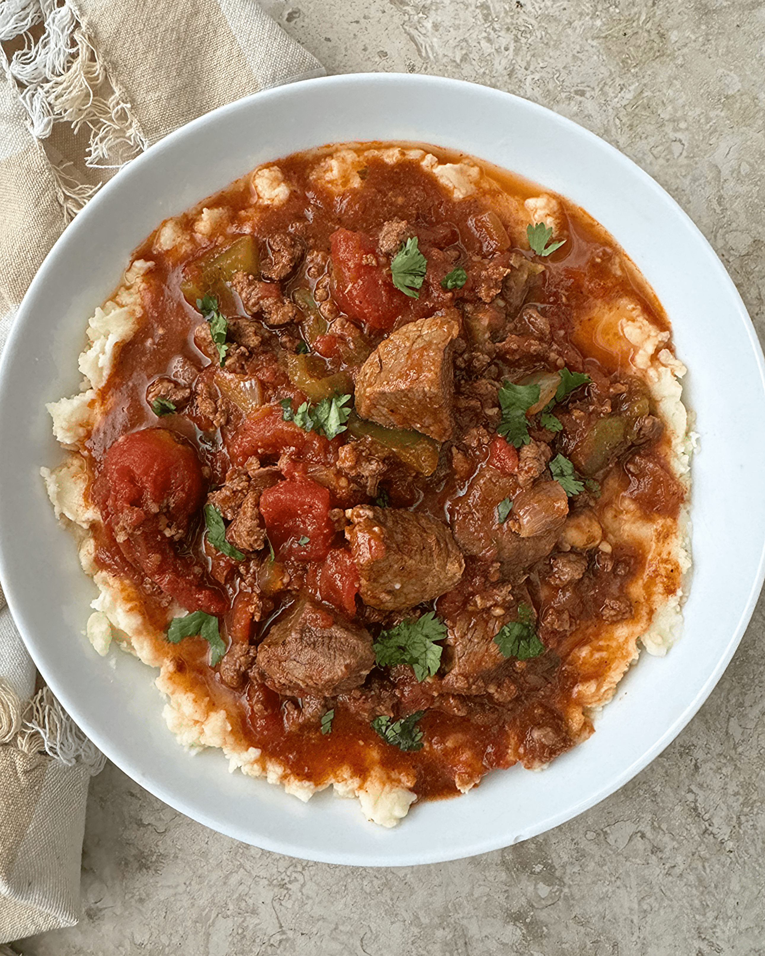 overhead shot of uncooked Beef Chili Stew served over mashed potatoes on a white plate