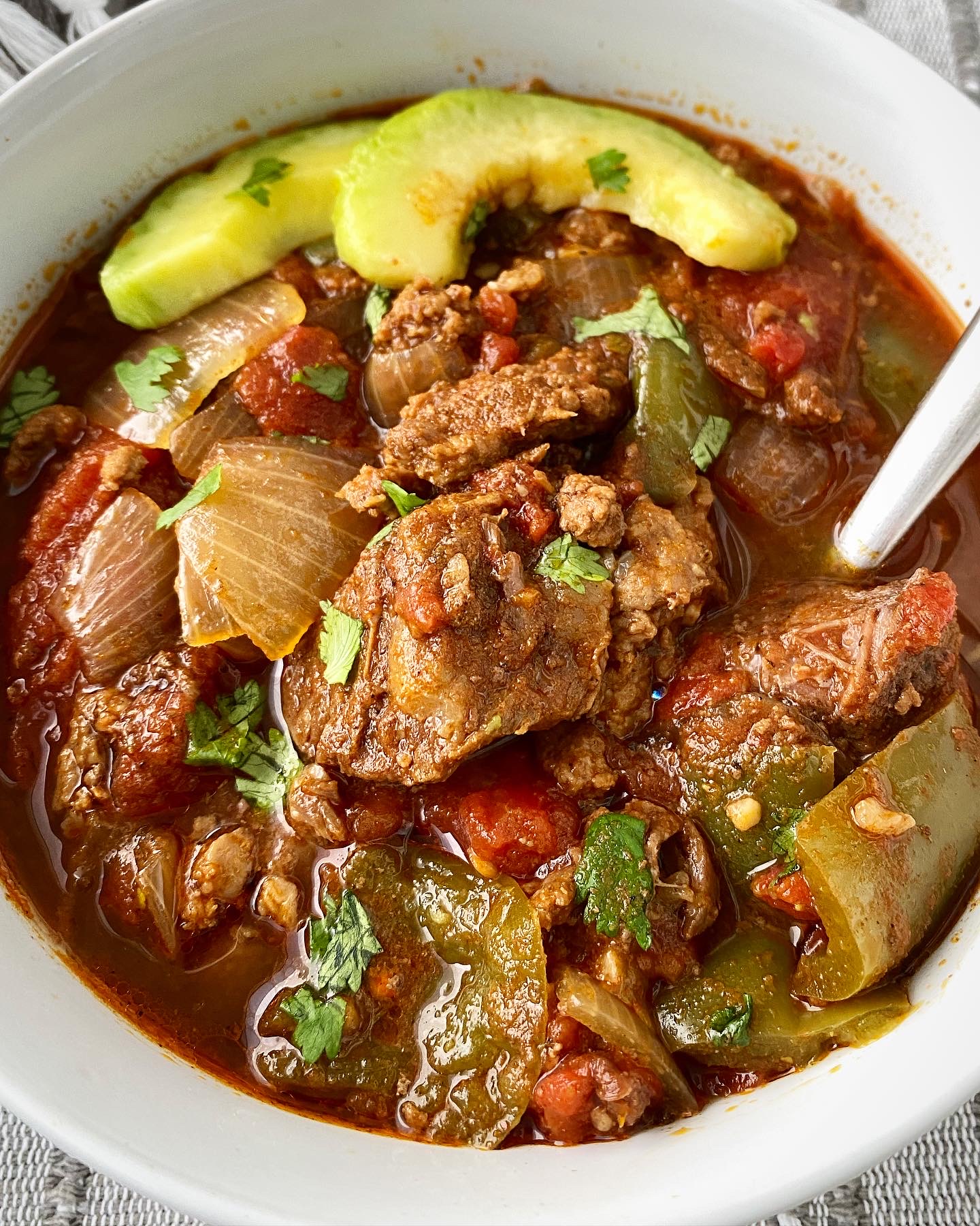 overhead shot of chunky beef stew in a white bowl garnish with avocado & cilantro