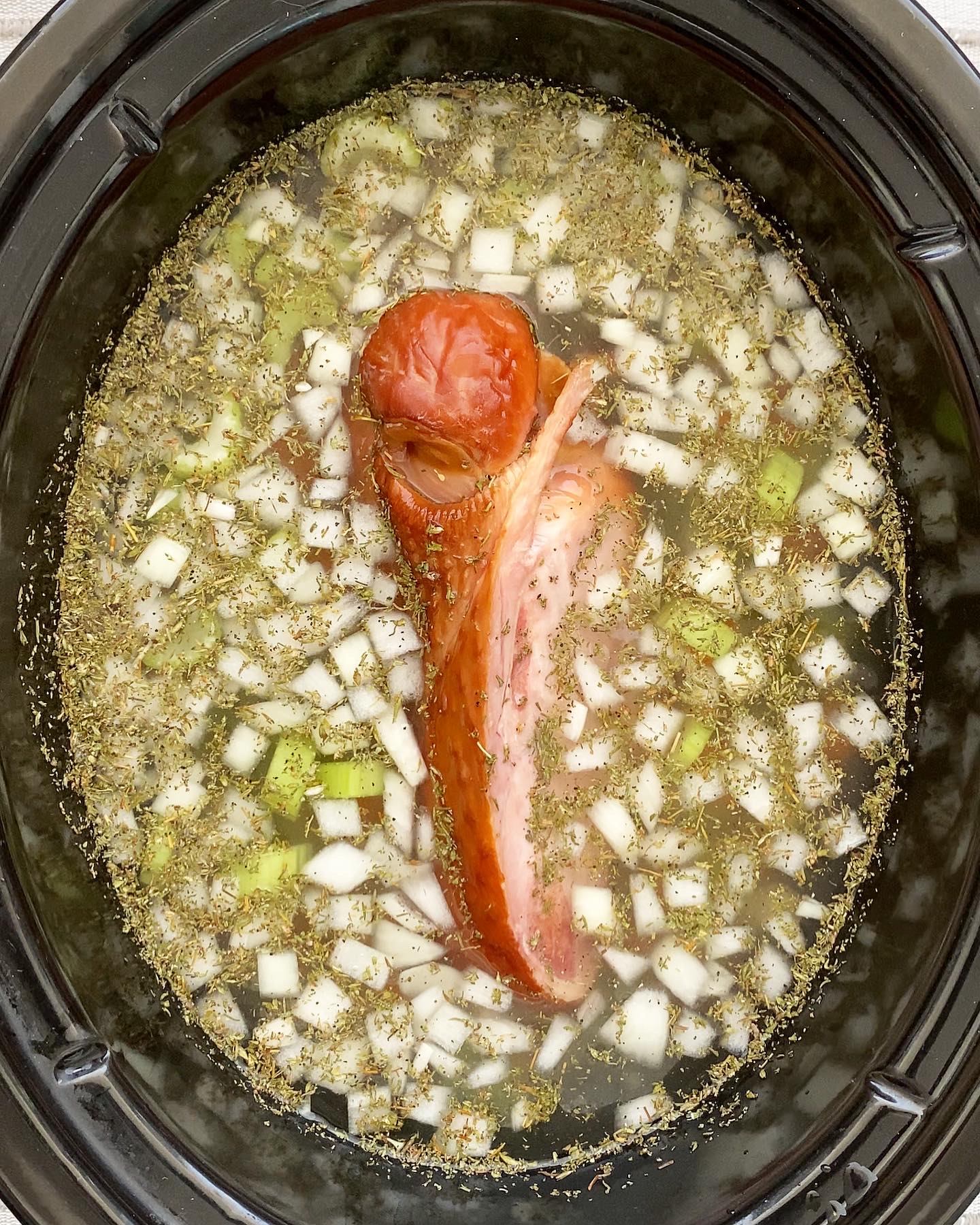 overhead shot of uncooked split pea soup in a black slow cooker with a turkey wing